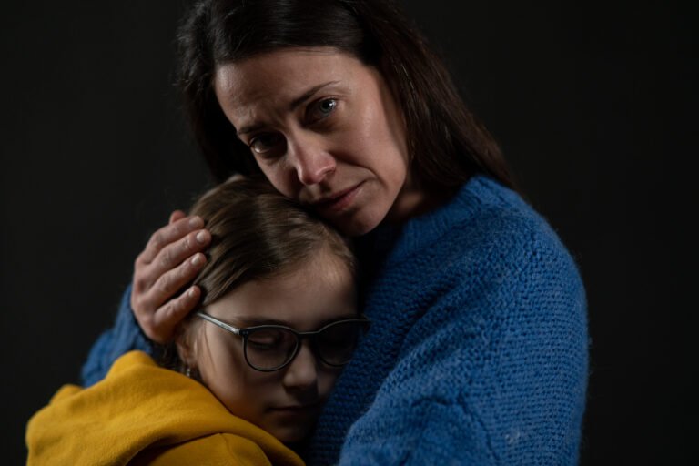 A mother embracing her daughter, both with sad expressions, wearing cozy sweaters.